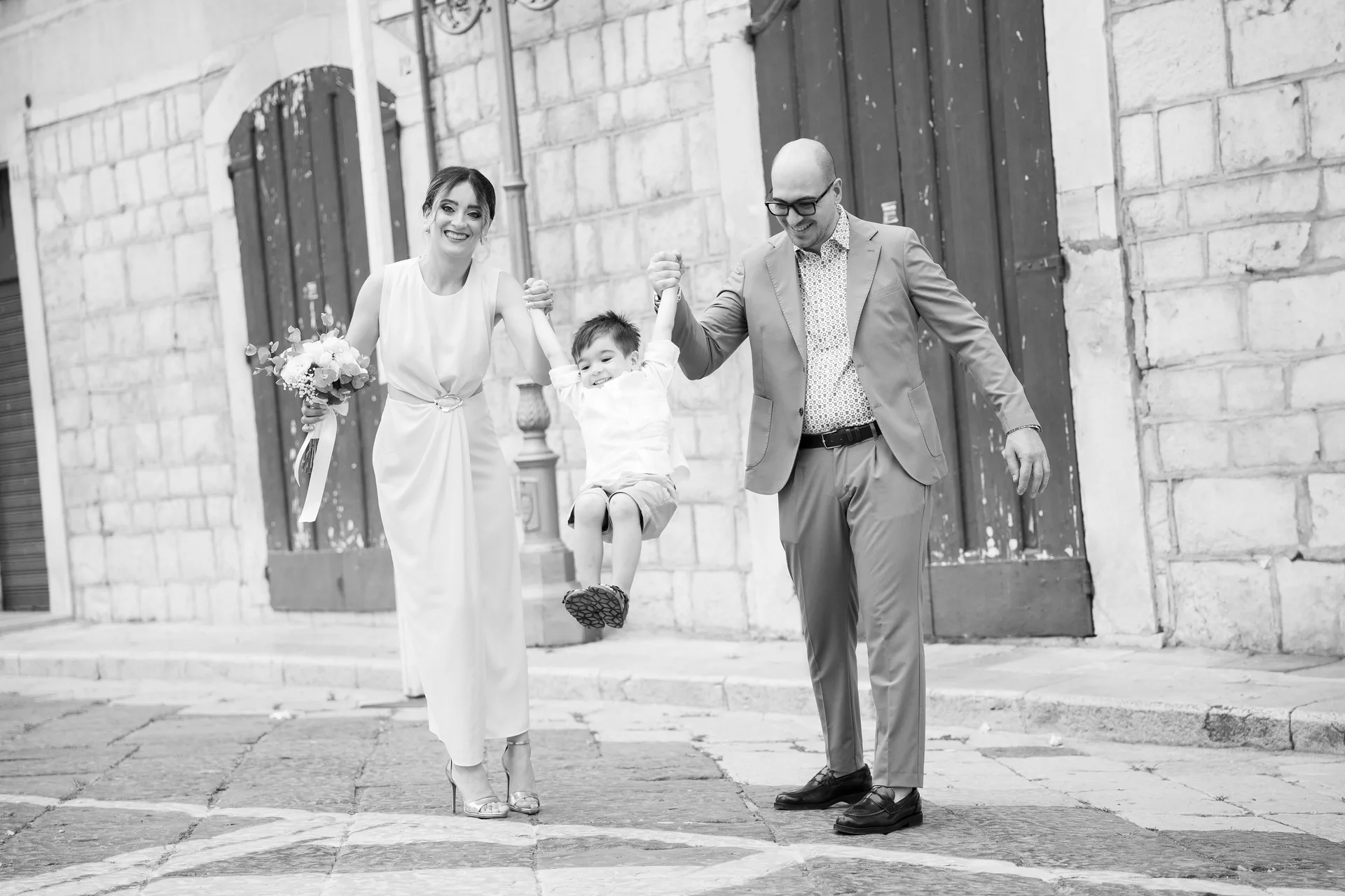 Gli sposi fanno volare il loro bambino tenendolo per mano davanti a un portale in pietra