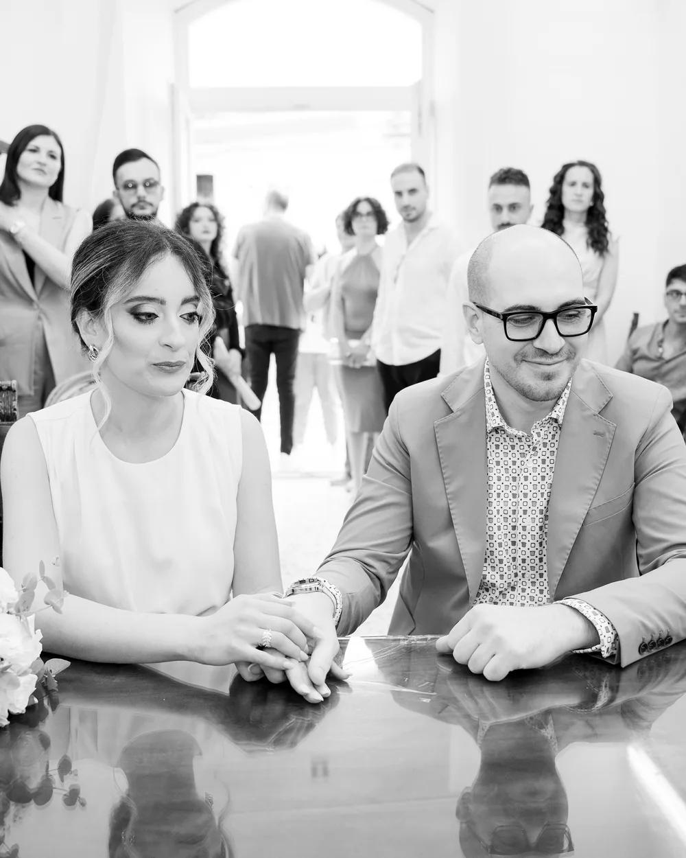 Gli sposi con le mani unite al tavolo, circondati dagli invitati