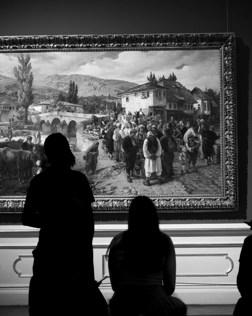 Visitatori in controluce davanti a un grande dipinto in un museo
